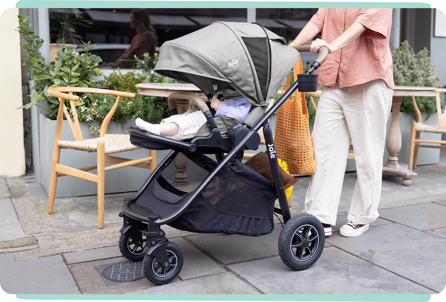 Zoomed in view of a mom pushing a baby in a Joie Versatrax pram and the canopy pulled low. 
