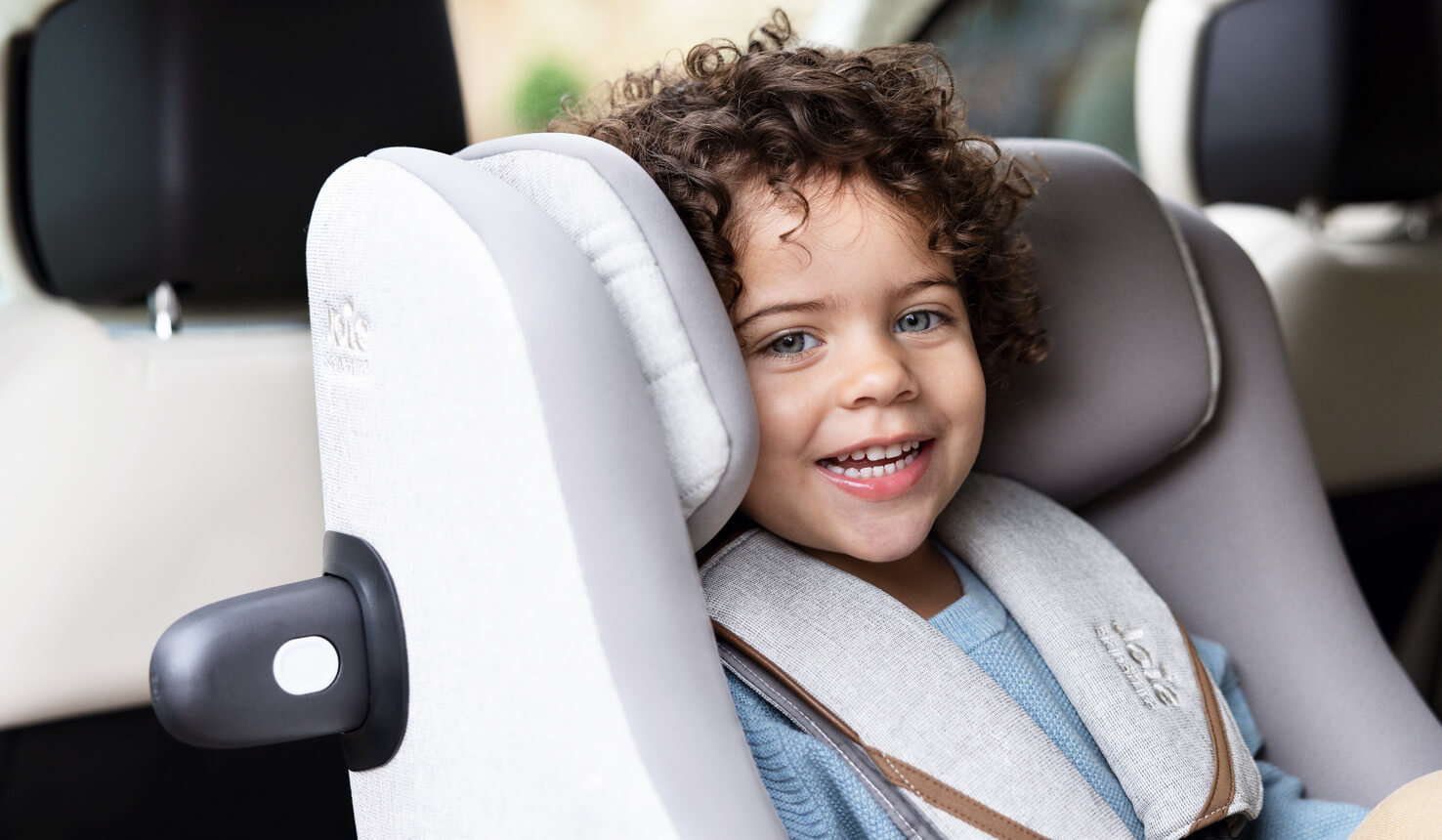 Primo piano di un bambino sorridente seduto nel seggiolino auto Joie i-Harbour grigio.