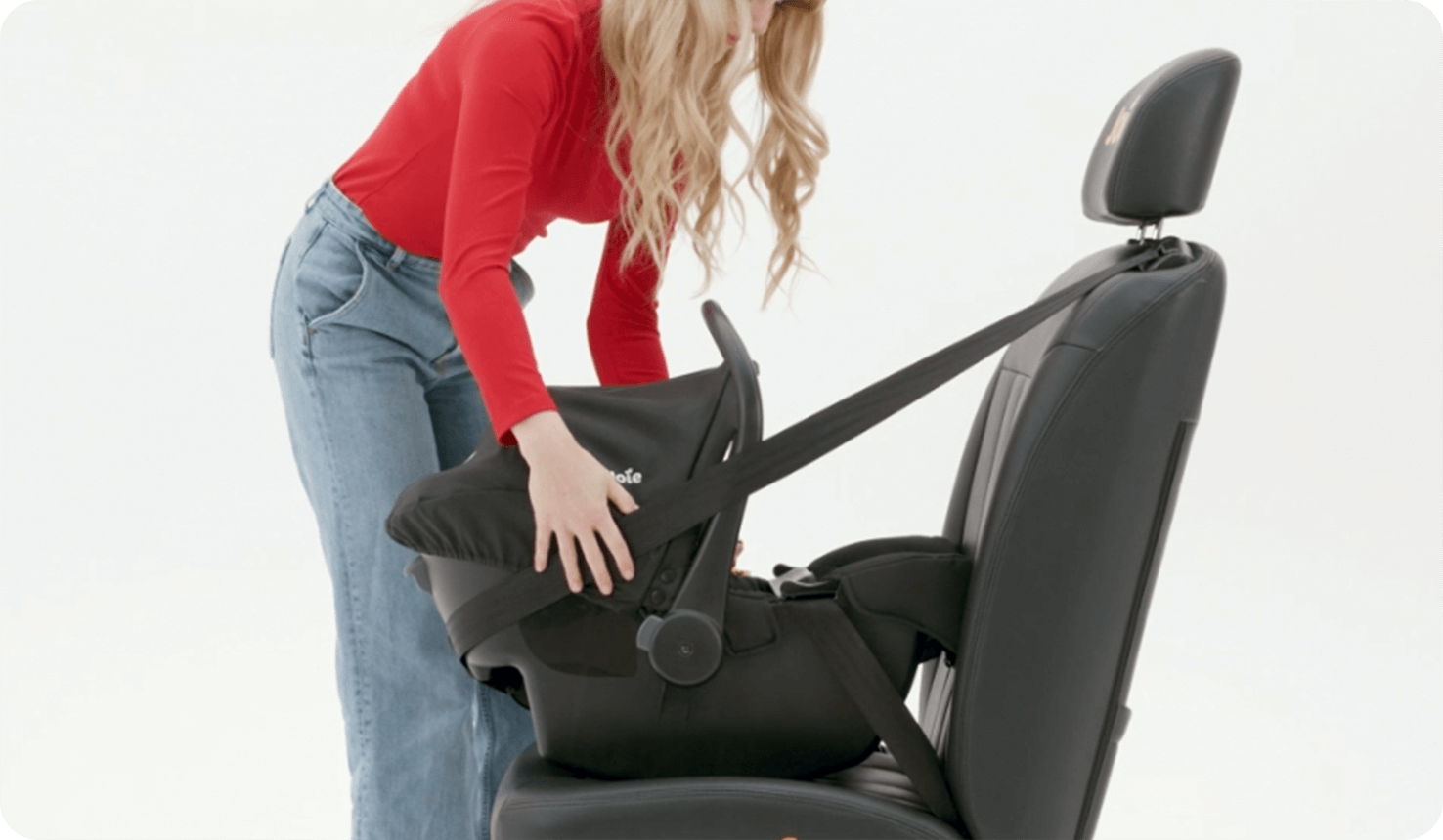 Mujer instalando la silla de coche para bebé Joie i-Juva en un asiento con el cinturón de seguridad.