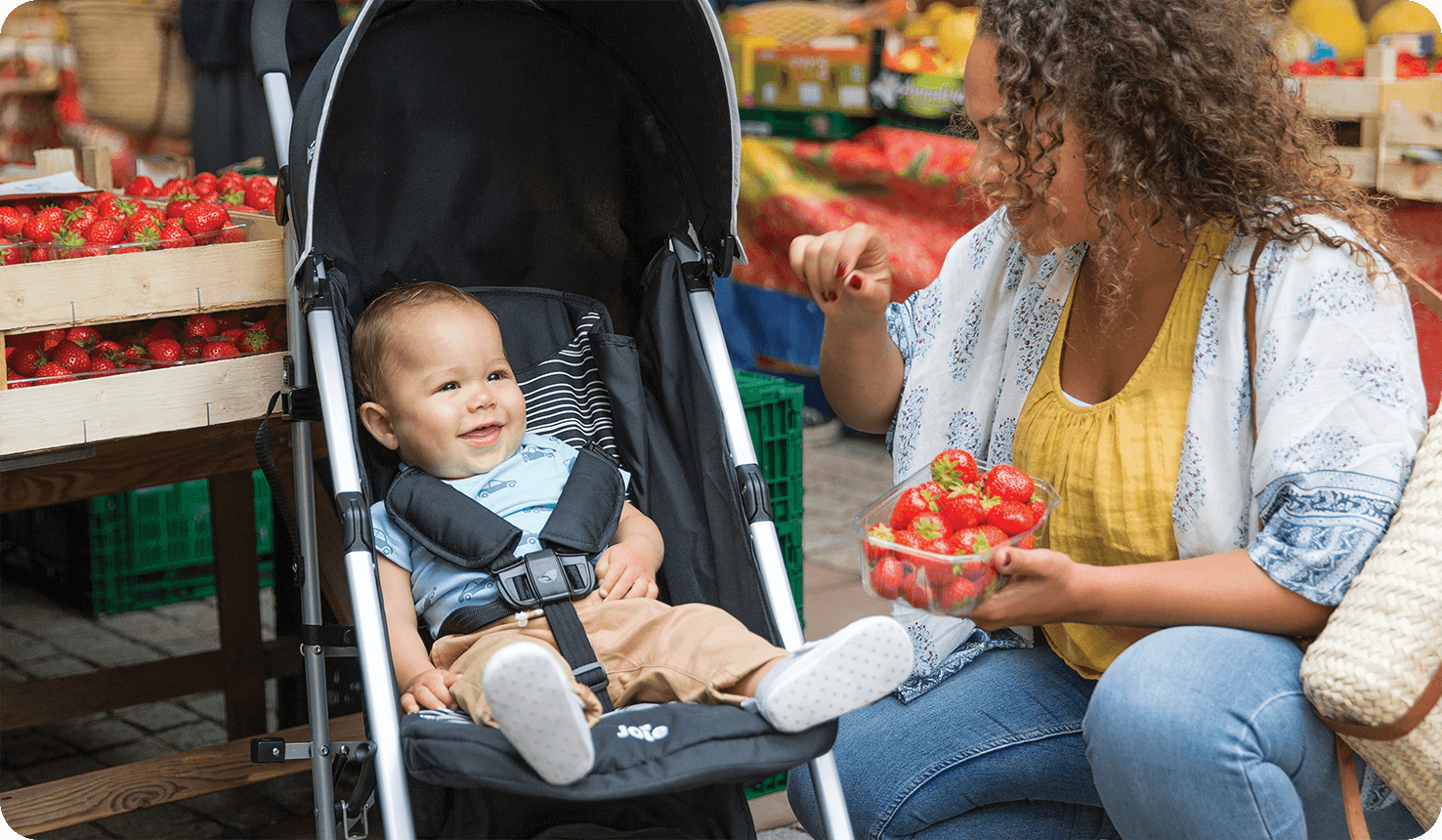   Mom kneeling next to baby sitting in Joie black and white rapid stroller.