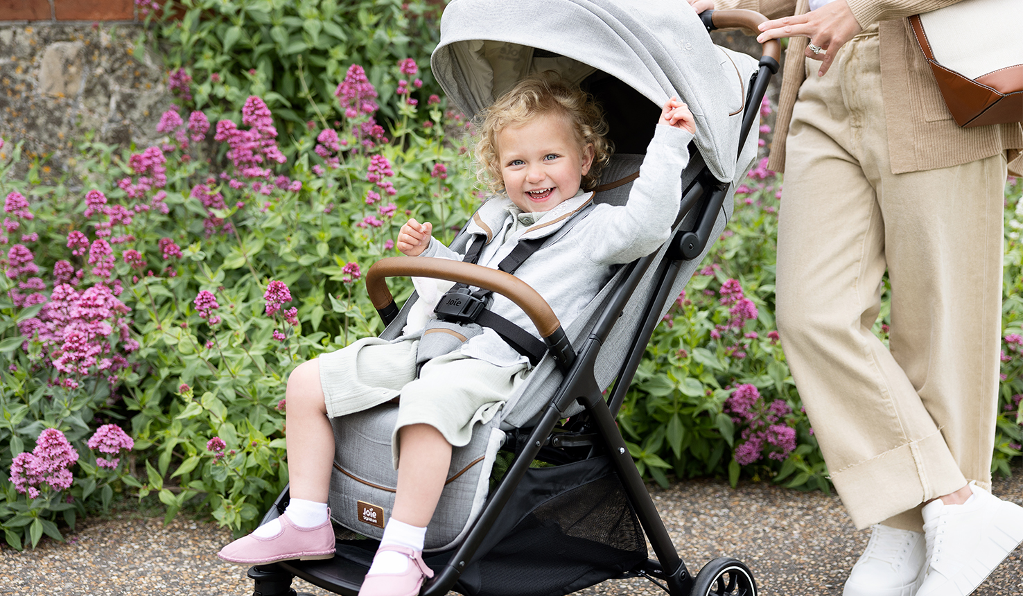 Bambina bionda sorridente seduta nel passeggino Joie Parcel.