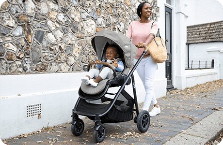 Mom kneeling to interact with young toddler in Joie Signature versatrax pram in gray