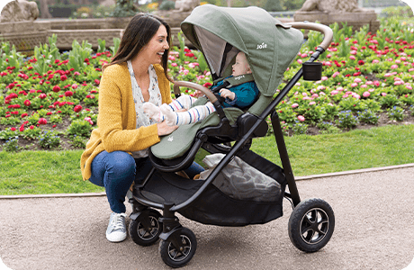 Mom kneeling to interact with young toddler in Joie Signature versatrax pram in light green.