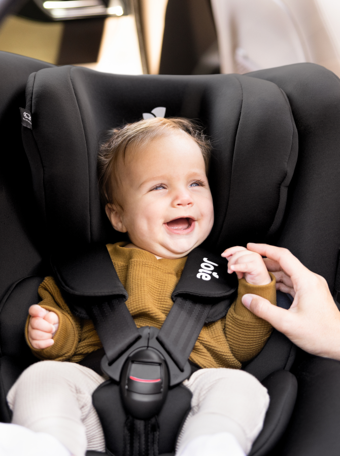 Bébé souriant installé dans un siège auto Joie i-spin 360 noir. 