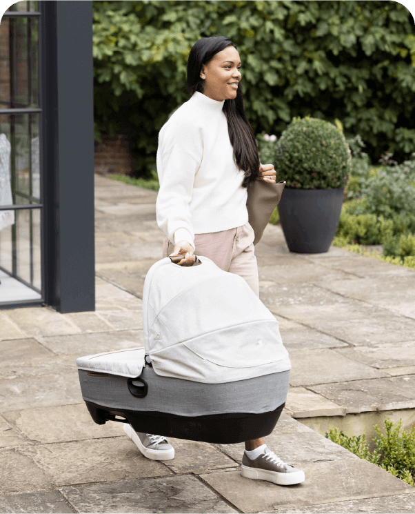 Donna che attraversa un patio trasportando la navicella omologata per l'auto Joie Calmi R129