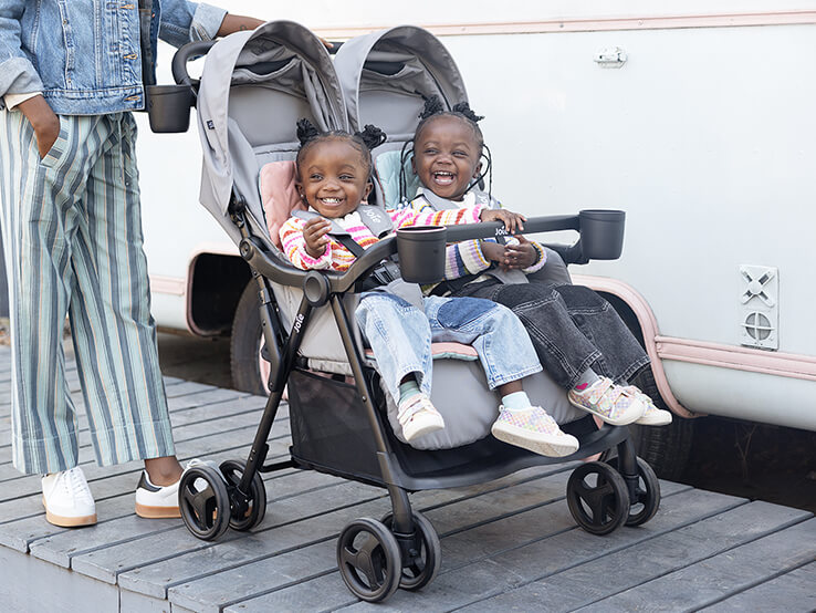 image of a mother with two kids smiling and laughing while sitting in a Joie stroller. 